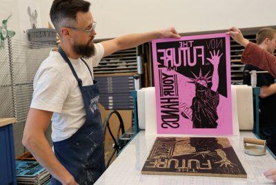 A man holds up a poster with the words “THE FUTURE YOUR HANDS” and a drawing of the Statue of Liberty.